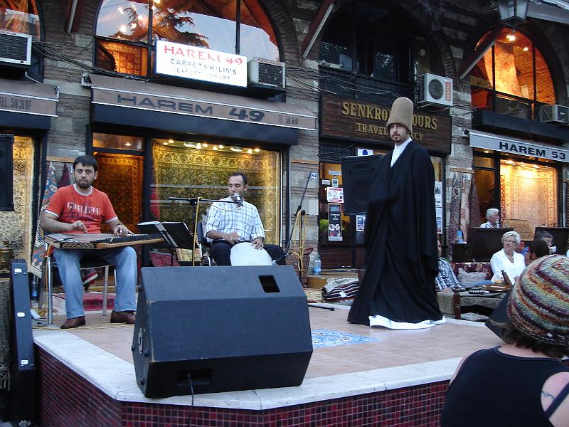 DSC01012.JPG - A Dervish, still in black cloak, prepares to whirl.  Many outdoor restaurants, such as this one, the Cafe Mesale, feature their own Dervish as part of the entertainment. 12 July 2007