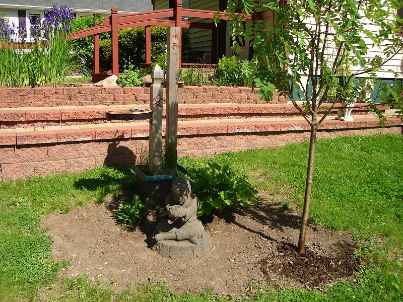 DSC01103.JPG - Our new mendicant in front of the bird baths.  Note Judy's Chinese calligraphy on the posts.  The short post has the character for "love" and the tall post has the characters for "peace", although Judy thinks the pattern she used has the peace characters reversed.  Andrew agrees, as does our Chinese dictionary, as well as the artwork hanging in our living room. 24 May 2009