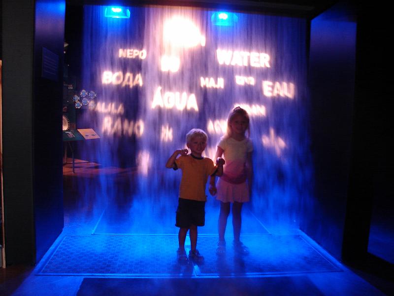 DSC00033.JPG - Two young people standing under some dry ice fog. like a waterfall, with words and images projected at the entrance to the Water. H2O =Life exhibit.  Natural History Museum San Diego. 8 August 2008